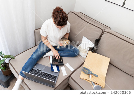 Woman budgeting pet expenses with a kitten using a laptop and calculator in living room Woman budgeting pet expenses with a kitten using a laptop and calculator in living room 142650366