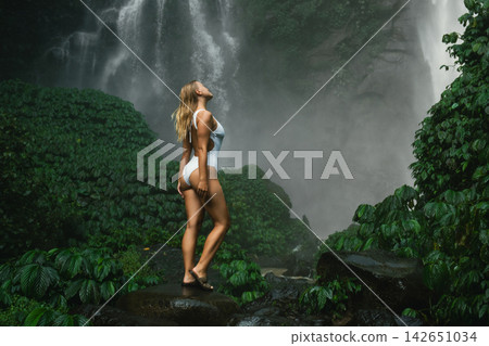 A person stands near a waterfall in Bali during a sunny day A person stands near a waterfall in Bali during a sunny day 142651034