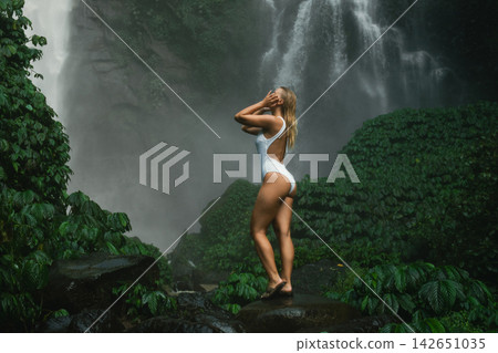 A model stands near a large waterfall surrounded by green plants A model stands near a large waterfall surrounded by green plants 142651035