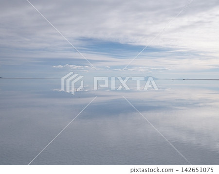 Bolivia's Uyuni Salt Flats: A breathtaking spectacle of the pale blue sky and white clouds reflected symmetrically on the mirror-like surface of the water. Bolivia's Uyuni Salt Flats: A breathtaking spectacle of the pale blue sky and white clouds reflected symmetrically on the mirror-like surface of the water. 142651075