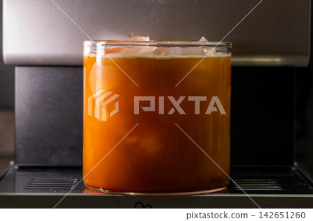 咖啡機將咖啡注入透明冰玻璃杯,在時間的光影中呈現永恆的冰淇淋、咖啡油和暖色光影。 咖啡機將咖啡注入透明冰玻璃杯,在時間的光影中呈現永恆的冰淇淋、咖啡油和暖色光影。 142651260