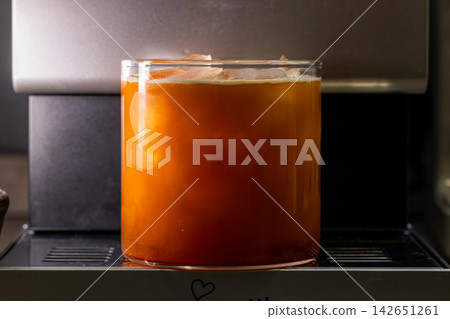 咖啡機將咖啡注入透明冰玻璃杯,在時間的光影中呈現永恆的冰淇淋、咖啡油和暖色光影。 咖啡機將咖啡注入透明冰玻璃杯,在時間的光影中呈現永恆的冰淇淋、咖啡油和暖色光影。 142651261