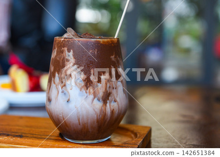 cocoa drink and chocolate - tasty milk shake with ice cocoa in glass on wood background cocoa drink and chocolate - tasty milk shake with ice cocoa in glass on wood background 142651384