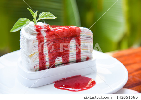 Crape cake slice with strawberry sauce on white plate and nature green background - Piece of cake rainbows with whipped cream Crape cake slice with strawberry sauce on white plate and nature green background - Piece of cake rainbows with whipped cream 142651569