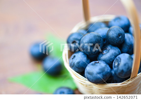 Fresh blueberries fruit in basket and green leaves on wooden background Fresh blueberries fruit in basket and green leaves on wooden background 142652071