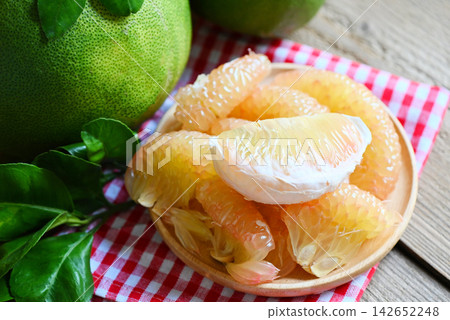 fresh green pomelo peeled and leaf frome pomelo tree , pummelo , grapefruit in summer tropical fruit in thailand , pomelo fruit on wooden plate background fresh green pomelo peeled and leaf frome pomelo tree , pummelo , grapefruit in summer tropical fruit in thailand , pomelo fruit on wooden plate background 142652248