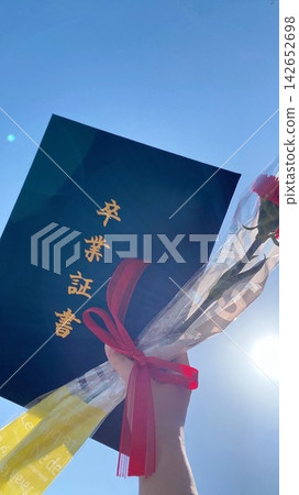 A graduation certificate and bouquet held up against the blue sky. A graduation certificate and bouquet held up against the blue sky. 142652698