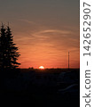 The horizon is painted in a vibrant orange hue, and the sun is setting. 142652907