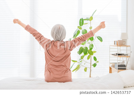 清晨，一位老婦人在床上伸展雙臂。這是充滿活力的醒來，也是老年人健康的一種形象。 142653737