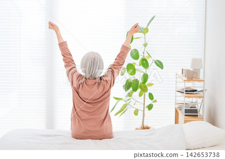 清晨,一位老婦人在床上伸展雙臂。這是充滿活力的醒來,也是老年人健康的一種形象。 清晨,一位老婦人在床上伸展雙臂。這是充滿活力的醒來,也是老年人健康的一種形象。 142653738