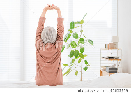 清晨，一位老婦人在床上伸展雙臂。這是充滿活力的醒來，也是老年人健康的一種形象。 142653739
