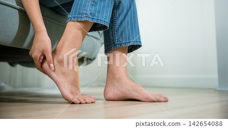 Asian young woman sitting on sofa holding her feet and stretch muscles have symptoms Asian young woman sitting on sofa holding her feet and stretch muscles have symptoms 142654088