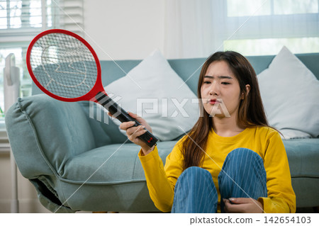 Asian female sitting floor using mosquito device swatter or electric net racket Asian female sitting floor using mosquito device swatter or electric net racket 142654103