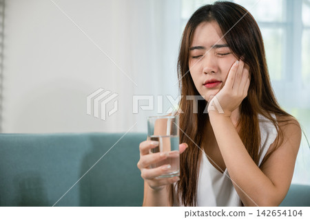 Beautiful female toothache and dental problems touching cheek feeling pain after drinking cold water 142654104