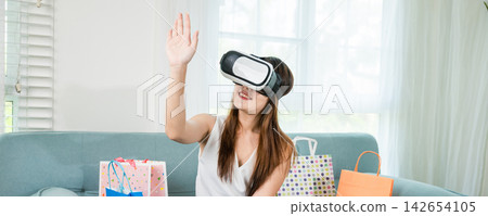 woman with shopping bags around wearing modern virtual reality headsets having experience in shopping online 142654105