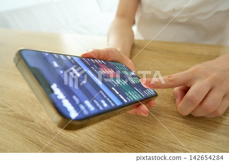 一位女士正在用智慧型手機查看股票價格,她的雙手在鏡頭前。 一位女士正在用智慧型手機查看股票價格,她的雙手在鏡頭前。 142654284