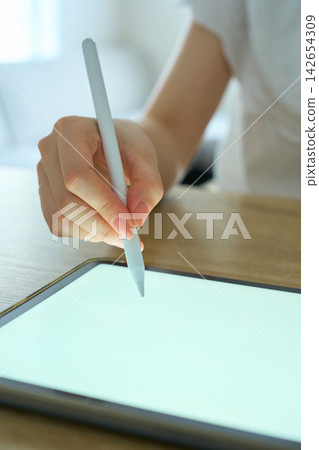 A young woman's hands as she operates a tablet. A young woman's hands as she operates a tablet. 142654309