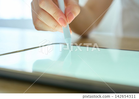 A young woman's hands as she operates a tablet. A young woman's hands as she operates a tablet. 142654311