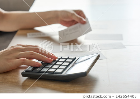 一位女士正在用計算機計算收據上的數字。 142654403