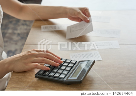 一位女士正在用計算機計算收據上的數字。 一位女士正在用計算機計算收據上的數字。 142654404