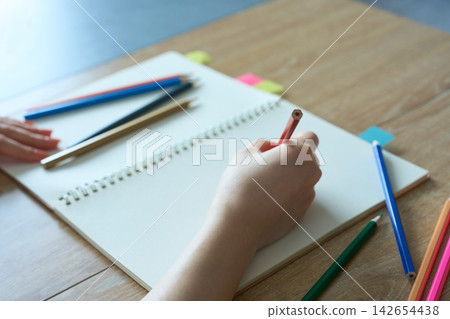 A woman's hands drawing in a sketchbook with colored pencils. A woman's hands drawing in a sketchbook with colored pencils. 142654438