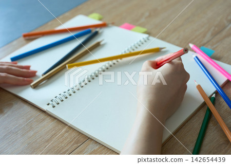 一位女士的手正在素描本上用色鉛筆畫畫。 一位女士的手正在素描本上用色鉛筆畫畫。 142654439