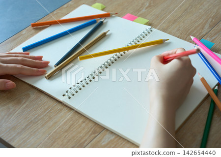 一位女士的手正在素描本上用色鉛筆畫畫。 一位女士的手正在素描本上用色鉛筆畫畫。 142654440