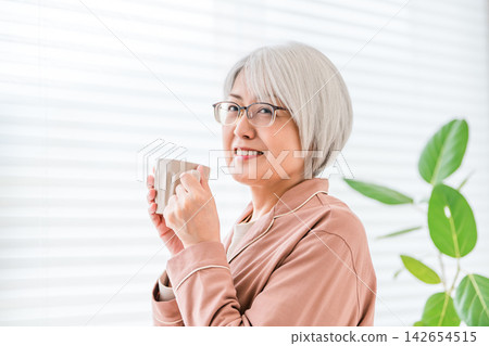 一位老婦人面帶微笑,手裡拿著一杯飲料。畫面展現了她健康充實的退休生活,她正在享受屬於自己的時光。 一位老婦人面帶微笑,手裡拿著一杯飲料。畫面展現了她健康充實的退休生活,她正在享受屬於自己的時光。 142654515