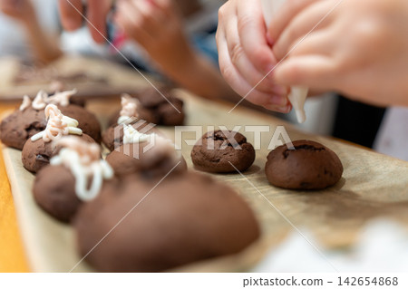 A photo of a child decorating chocolate cookies with white and light brown icing. A photo of a child decorating chocolate cookies with white and light brown icing. 142654868