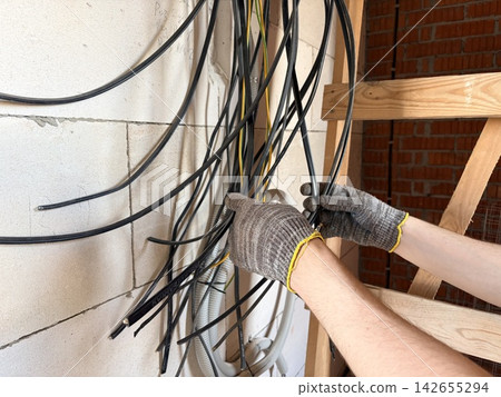 An electrician's hands lay electrical cables into a wall. A building renovation or construction project. An electrician's hands lay electrical cables into a wall. A building renovation or construction project. 142655294