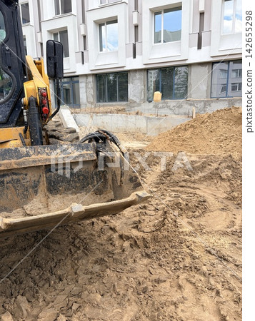 A metal construction bucket rests on a mound of loose, lumpy soil and sand. A metal construction bucket rests on a mound of loose, lumpy soil and sand. 142655298