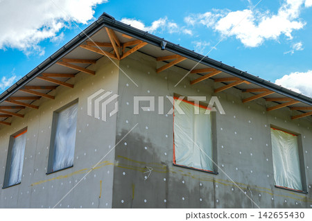 Modern House Facade with Thermal Insulation and Unfinished Roof Eaves Under Construction Modern House Facade with Thermal Insulation and Unfinished Roof Eaves Under Construction 142655430