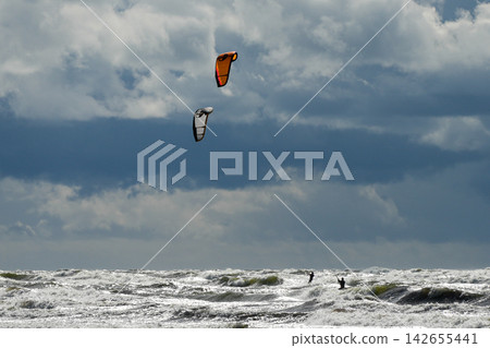 Two Kitesurfers Riding Rough Baltic Sea Waves Under Dramatic Storm Clouds on Windy Day Two Kitesurfers Riding Rough Baltic Sea Waves Under Dramatic Storm Clouds on Windy Day 142655441