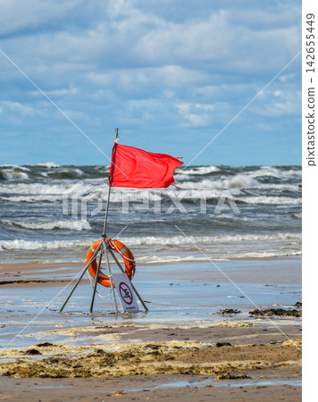 Red Warning Flag and Lifebuoy on Stormy Baltic Sea Beach During Dangerous Rough Sea Conditions Red Warning Flag and Lifebuoy on Stormy Baltic Sea Beach During Dangerous Rough Sea Conditions 142655449