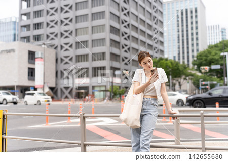 一位穿著休閒的女子在等人時正在查看智慧型手機。 一位穿著休閒的女子在等人時正在查看智慧型手機。 142655680