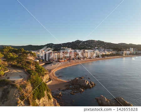 Aerial view taken from a drone of the coast of Lloret de Mar, Costa Brava, Spain, early in the morning at sunrise - the sea, beach and coastal hotels Aerial view taken from a drone of the coast of Lloret de Mar, Costa Brava, Spain, early in the morning at sunrise - the sea, beach and coastal hotels 142655828