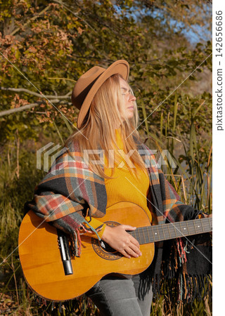 Blonde woman playing string guitar outdoors in autumn forest. Concept of sound therapy, mental health and wellness rituals. Calmness tranquility audio-sensory practices. Aura farming energy Blonde woman playing string guitar outdoors in autumn forest. Concept of sound therapy, mental health and wellness rituals. Calmness tranquility audio-sensory practices. Aura farming energy 142656686