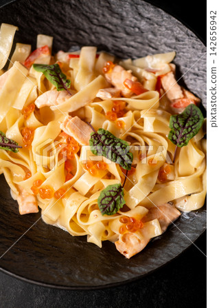Creamy tagliatelle. Italian cuisine. Appetizing dish with salmon red caviar in sauce. Tasty meal garnished with small sorrel leaves. Creamy tagliatelle. Italian cuisine. Appetizing dish with salmon red caviar in sauce. Tasty meal garnished with small sorrel leaves. 142656942