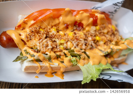 Fast food. Hot dog. Street meal in bun with sausage cheese sauce onions corn kernels tomato slices lettuce served in paper tray for takeout. Fast food. Hot dog. Street meal in bun with sausage cheese sauce onions corn kernels tomato slices lettuce served in paper tray for takeout. 142656958