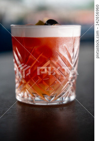 Alcohol drink. Aperitif glass. Bright red new york sour cold bright cocktail with white foam garnished with olive on dark pub counter. Alcohol drink. Aperitif glass. Bright red new york sour cold bright cocktail with white foam garnished with olive on dark pub counter. 142656960