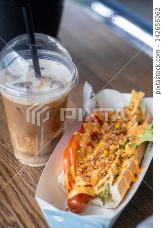 Takeaway meal. Street lunch. Hot dog sausage in bun with tomato lettuce sauce topping. Caffeine beverage with milk in closed disposable cup. Takeaway meal. Street lunch. Hot dog sausage in bun with tomato lettuce sauce topping. Caffeine beverage with milk in closed disposable cup. 142656962