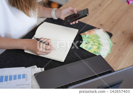 Woman planning household budget with cash and smartphone at home Woman planning household budget with cash and smartphone at home 142657403