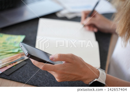 Woman checking household expenses with smartphone and notebook 142657404