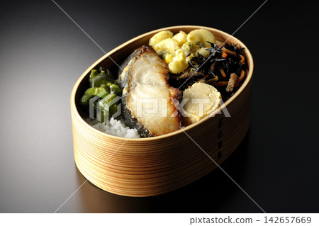 A bento box of grilled silver cod marinated in Saikyo miso, photographed against a black background. A bento box of grilled silver cod marinated in Saikyo miso, photographed against a black background. 142657669