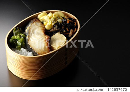 A bento box of grilled silver cod marinated in Saikyo miso, photographed against a black background. A bento box of grilled silver cod marinated in Saikyo miso, photographed against a black background. 142657670