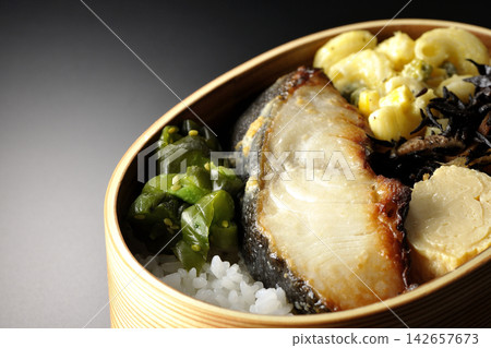 A bento box of grilled silver cod marinated in Saikyo miso, photographed against a black background. A bento box of grilled silver cod marinated in Saikyo miso, photographed against a black background. 142657673