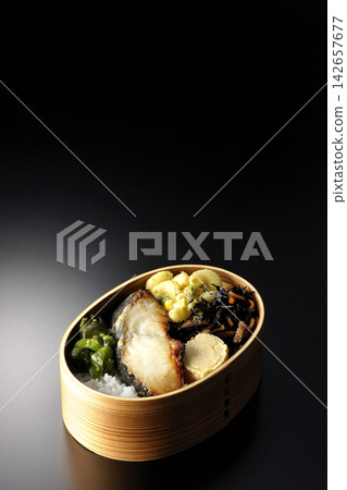 A bento box of grilled silver cod marinated in Saikyo miso, photographed against a black background. A bento box of grilled silver cod marinated in Saikyo miso, photographed against a black background. 142657677