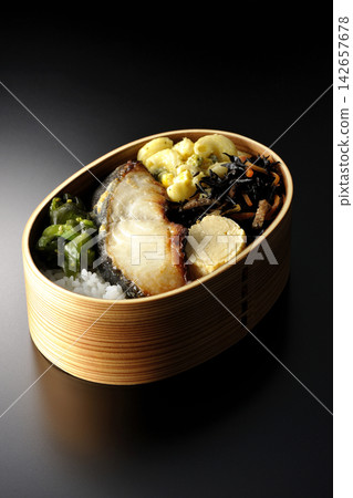A bento box of grilled silver cod marinated in Saikyo miso, photographed against a black background. A bento box of grilled silver cod marinated in Saikyo miso, photographed against a black background. 142657678