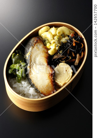 A bento box of grilled silver cod marinated in Saikyo miso, photographed against a black background. A bento box of grilled silver cod marinated in Saikyo miso, photographed against a black background. 142657700