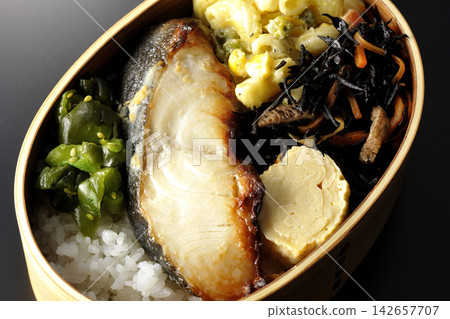 A bento box of grilled silver cod marinated in Saikyo miso, photographed against a black background. A bento box of grilled silver cod marinated in Saikyo miso, photographed against a black background. 142657707